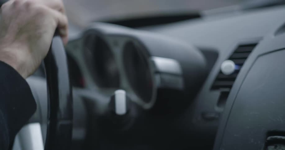 A man's hands turning a steering wheel on a moving car