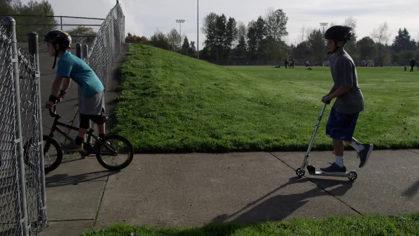 Children ride scooters and a bicycle in a park