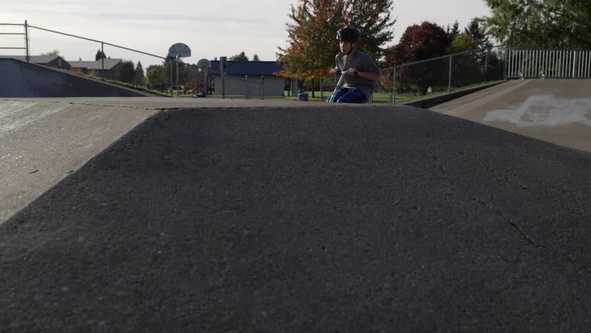 A boy rides a scooter in a skatepark