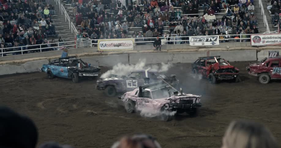 A large crowd watches as vehicles crash into each other at a car show