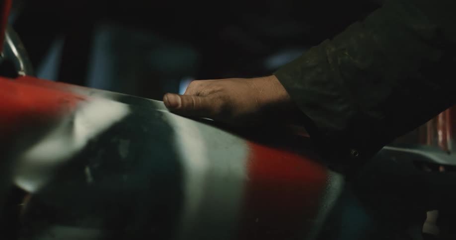 A man rubs a greasy hand along the fender of an automobile
