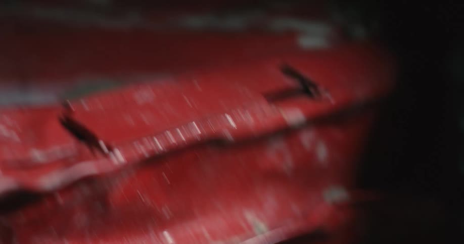 A mechanic uses his fist to pound on the wrecked fender and hood of a red car