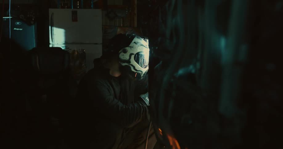 Sparks fly as a man wearing a helmet is welding in a dark room