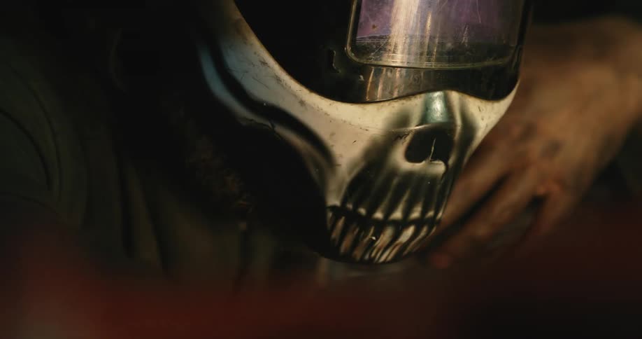 A man stands and watches as someone welding is reflected off a helmet