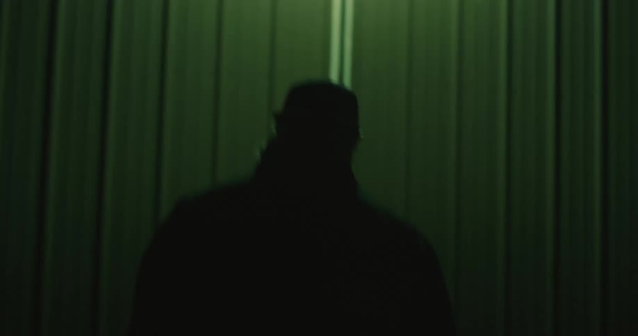 A man with a beard and wearing a cap walks to a garage at night and opens the door