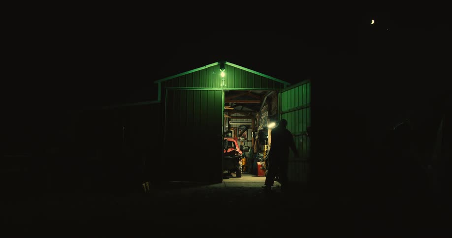A man opens the large doors of a garage workshop to show a car frame