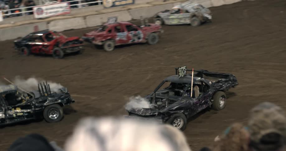 Cars crash and are smoking in a demolition derby as one car is moving in reverse and the other car appears to be chasing it