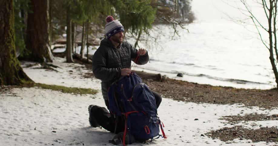 A man is fastening his backpack by the water