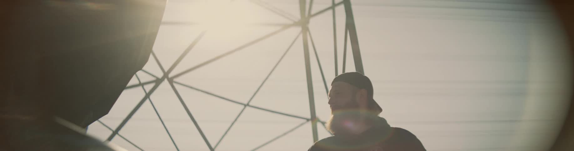 The sun is shining brightly up a man with a beard as he stands near a utility tower