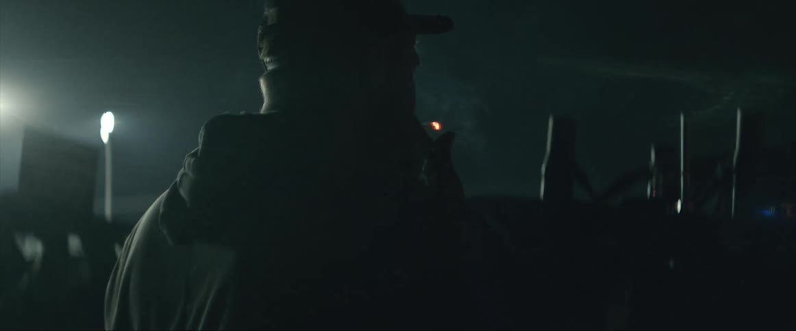 A man tilts his head back after lighting a cigarette while hanging out with friends in a lot of cars