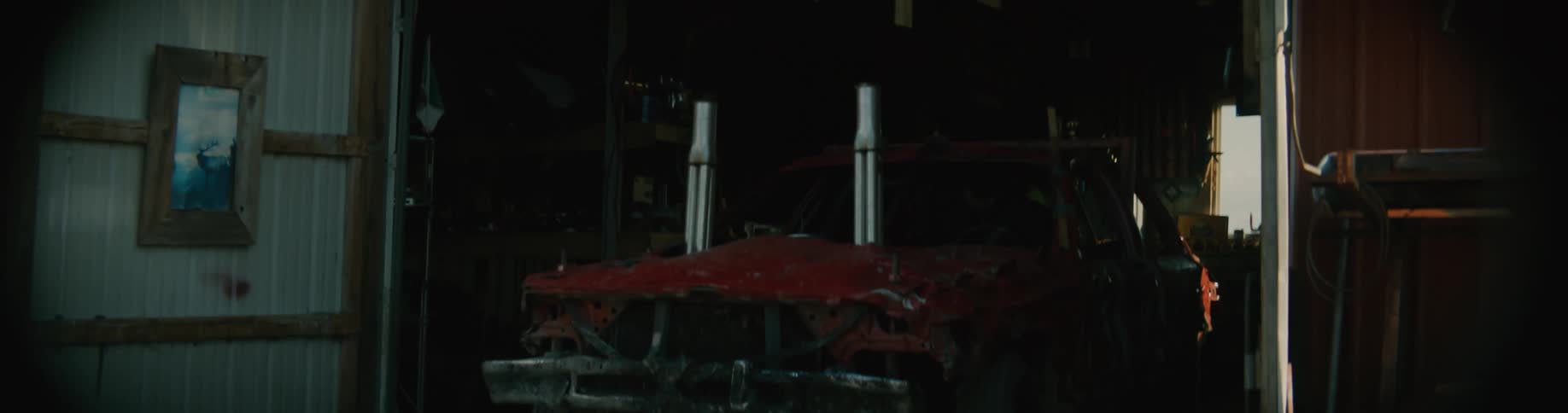 A red demolition derby automobile backs into a garage