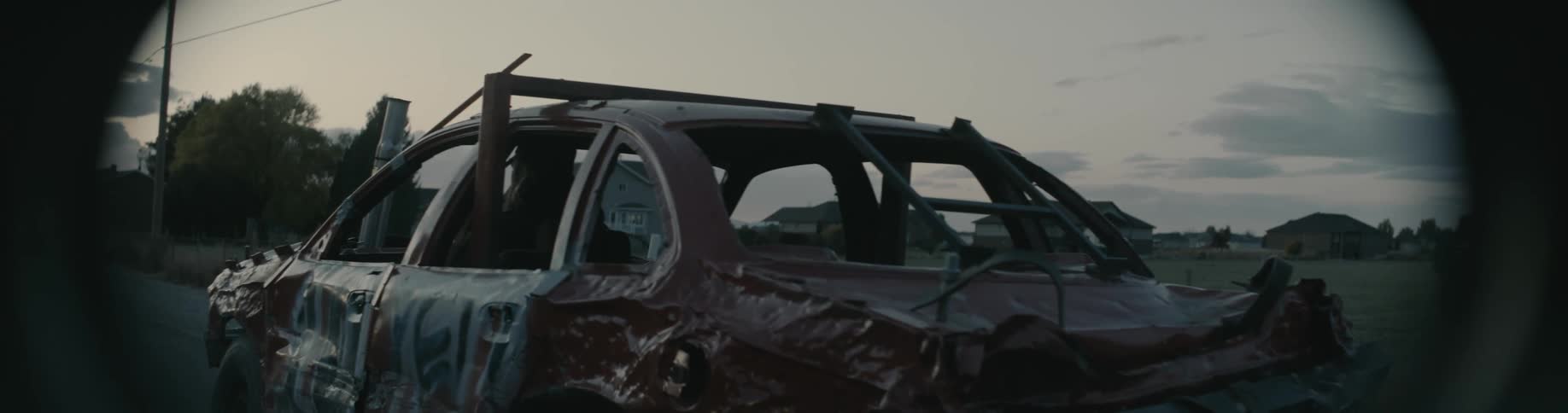 A man drives a demolition derby car down a street towards a neighborhood