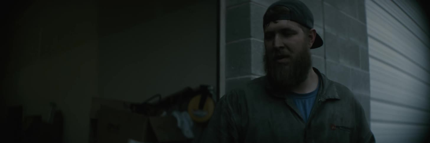 A mechanic in coveralls follows another man past a garage bay
