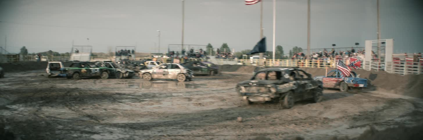 Cars drive around muddy arena and crash into each other at demo derby as crowd watches