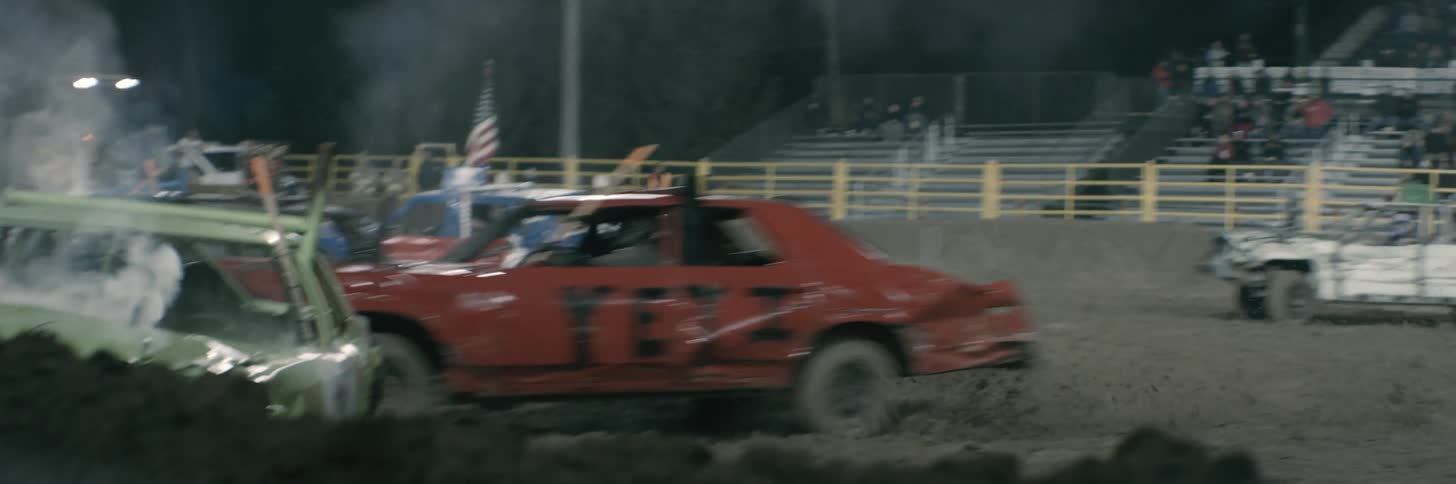 A car in a dirt stadium revs and rams into another during a demolition derby