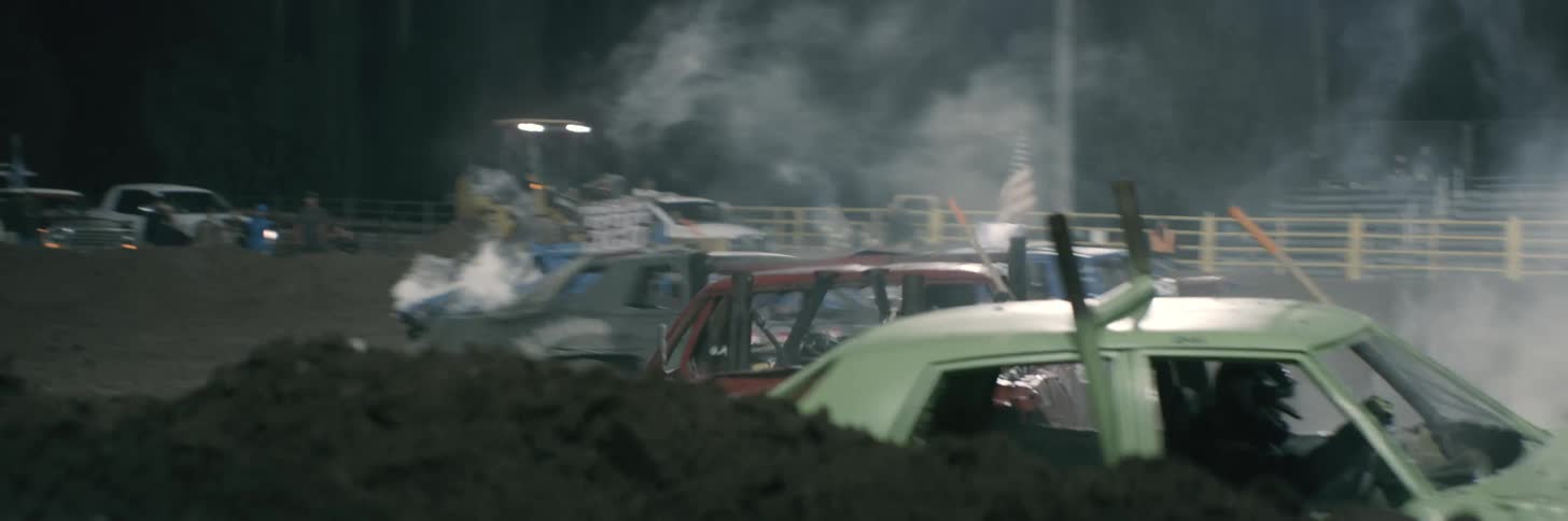 Red vehicle at demolition derby drives across dirt arena