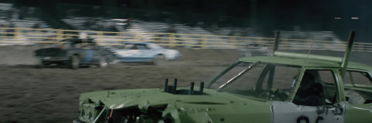 Old junk race cars are moving around an arena crashing into each other in a demolition derby