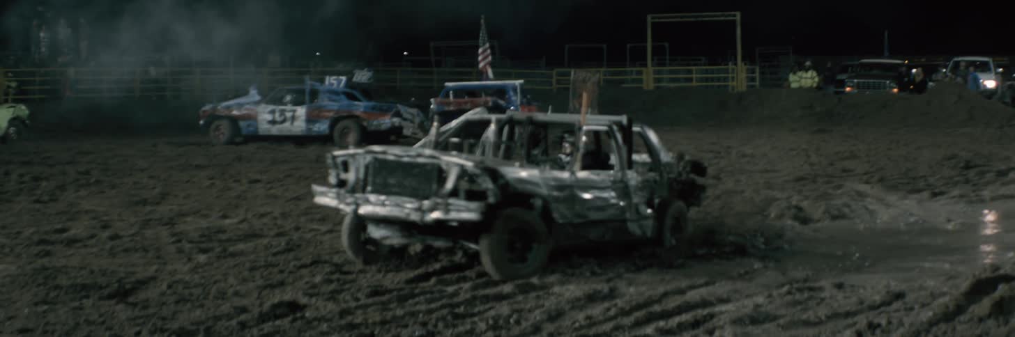A man is doing donuts in a beat up race car on a dirt track in an arena