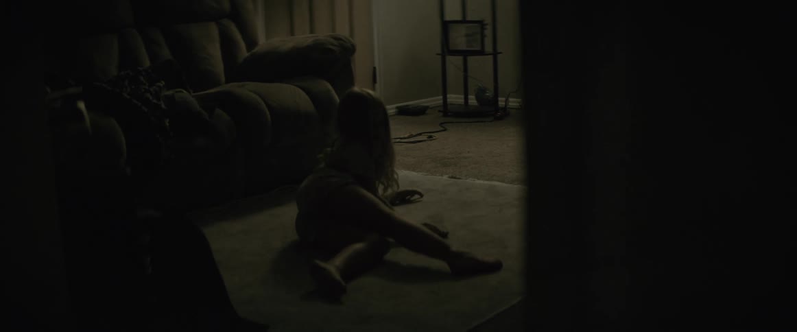A dad walks past his daughter in the living room as she gets down on the rug to play with a toy car