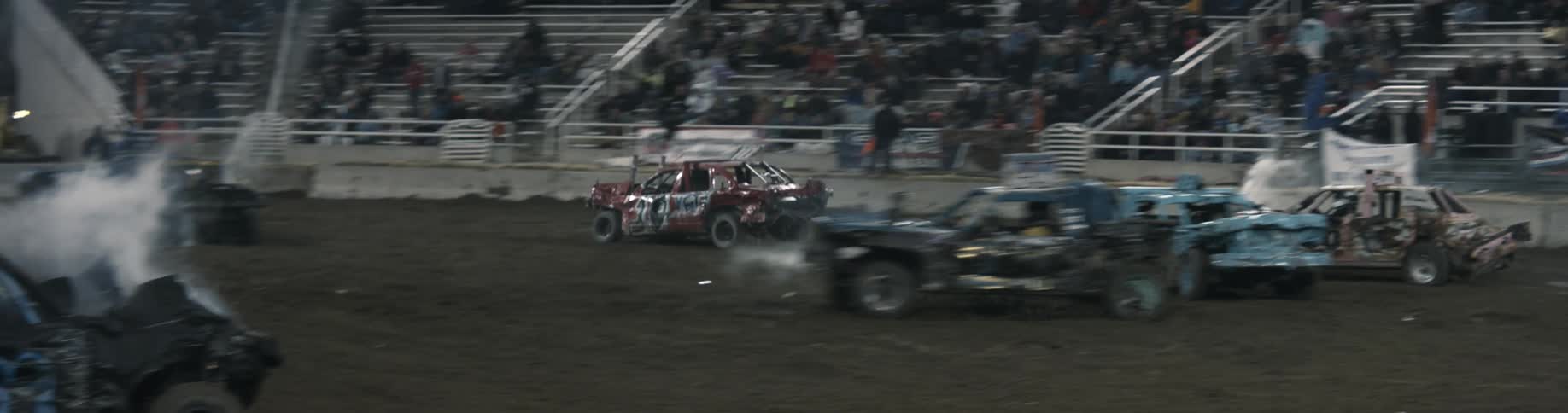 Spectators sit in the stands and watch as cars crash in to each other at a demolition derby