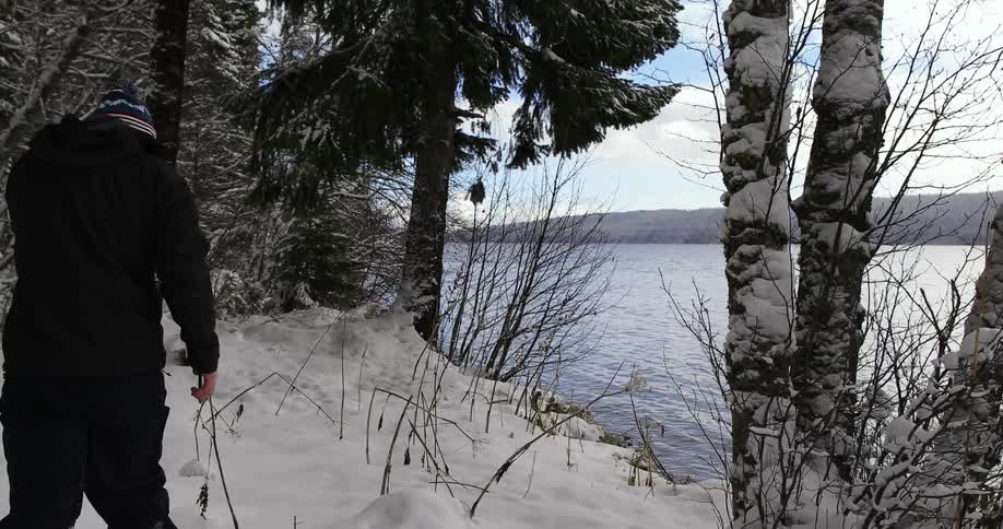A man walks through the snow next to a lake