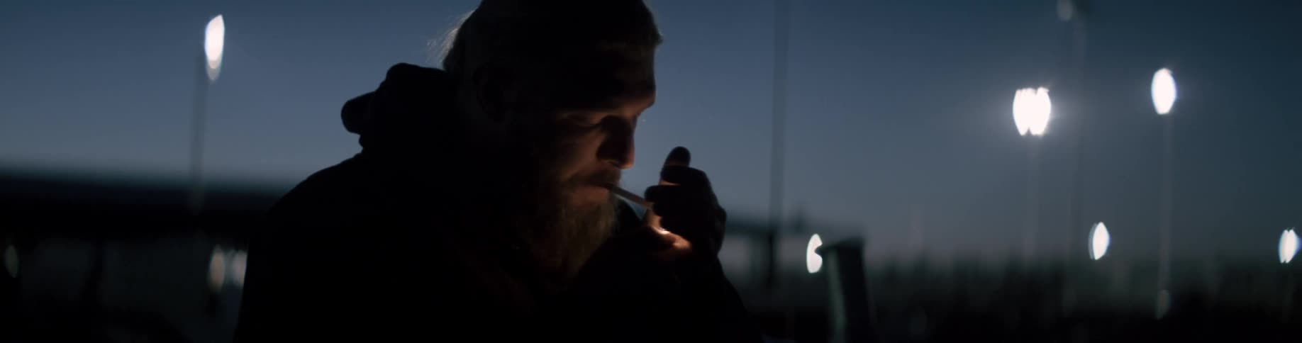A man is smoking a cigarette and standing outdoors at night