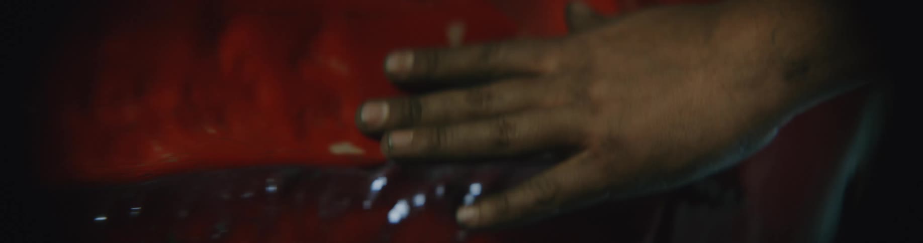 A black person moves their hand across the smashed body of a red automobile