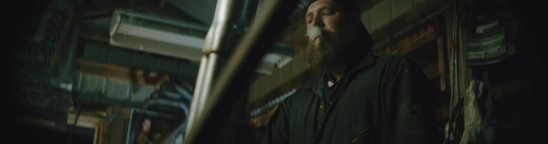 A man is standing inside an unfinished interior of a building and smoking a cigarette