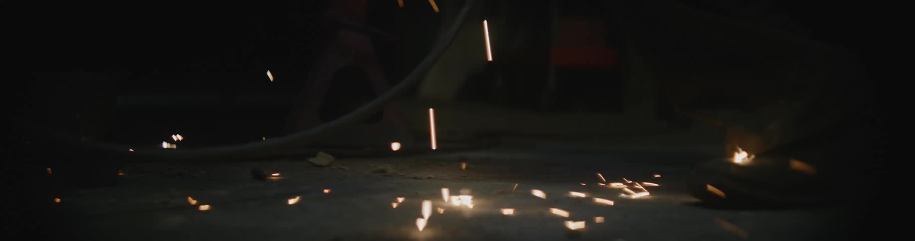 A man is in a dark room welding and throwing sparks