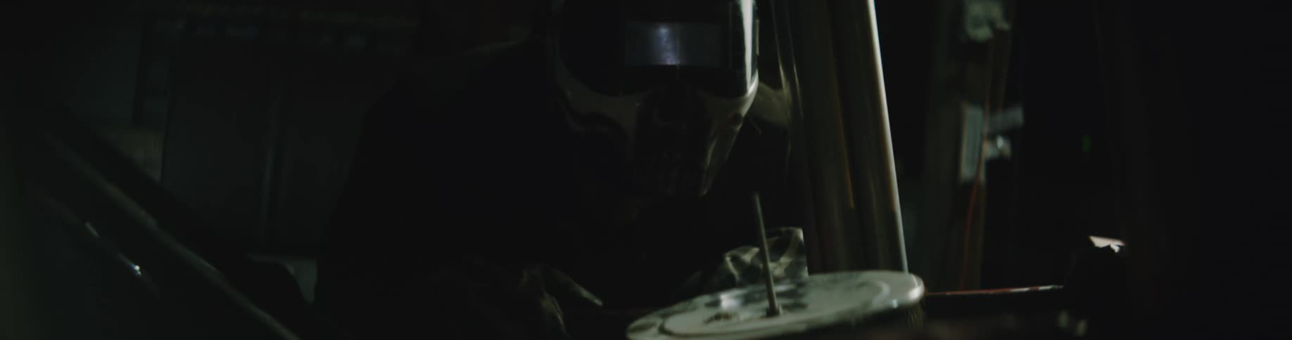 A man with a beard and wearing a helmet is looking at parts in a dark garage