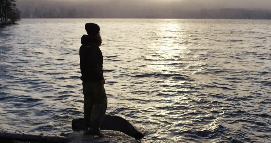 Woman stands on a rock overlooking a mountain lake
