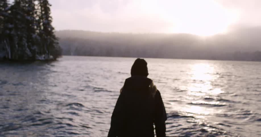 A woman walks towards the water at sunset