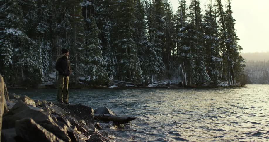 A woman stands on a rock near a river