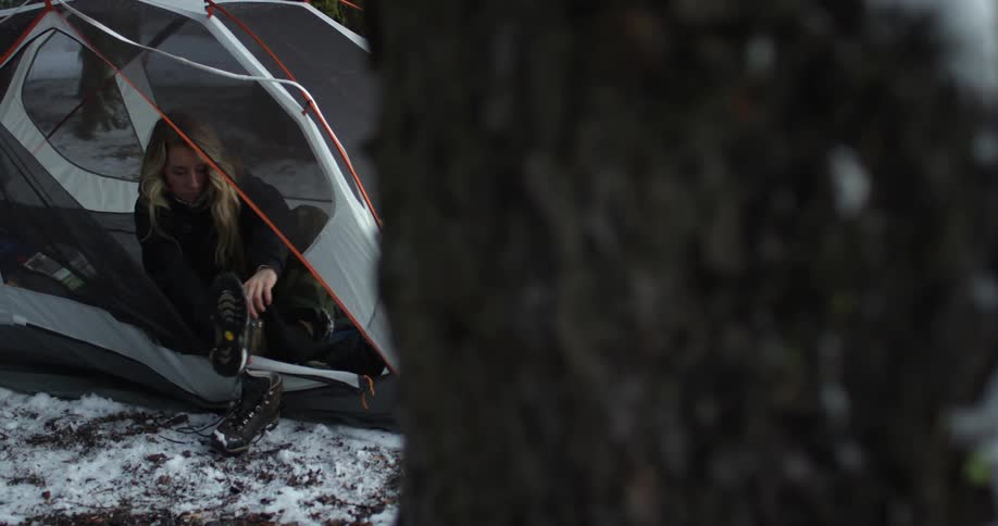 Woman unzips a tent and puts on the boots that are sitting outside