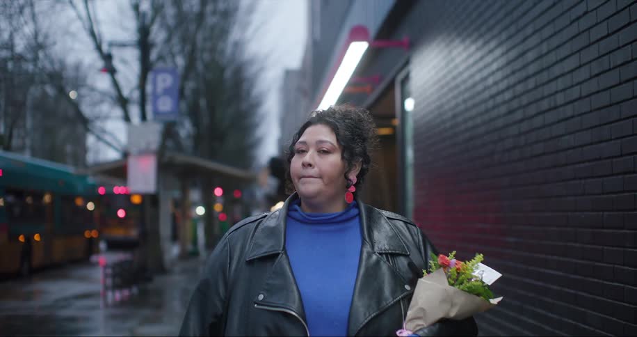 A woman walks down a city street holding a bouquet of flowers