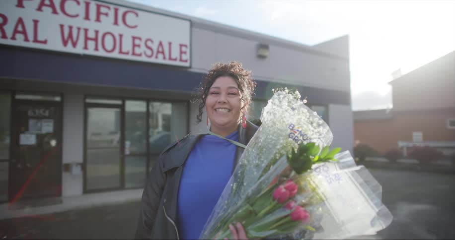 Happy woman standing in front of floral shop holding flowers