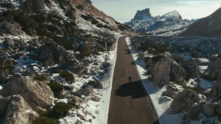 Cyclist rides bicycle along highway through snow covered mountains terrain
