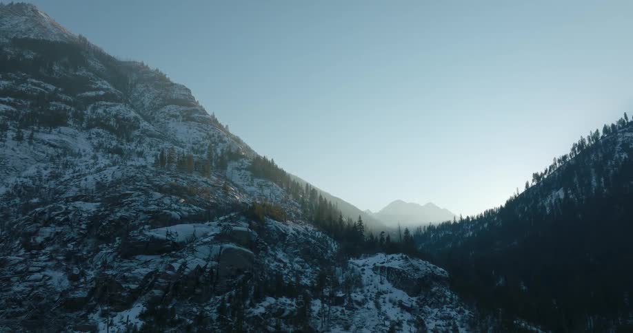 Traverse along a rocky mountain valley as the last rays of sun illuminate mountains in the distance