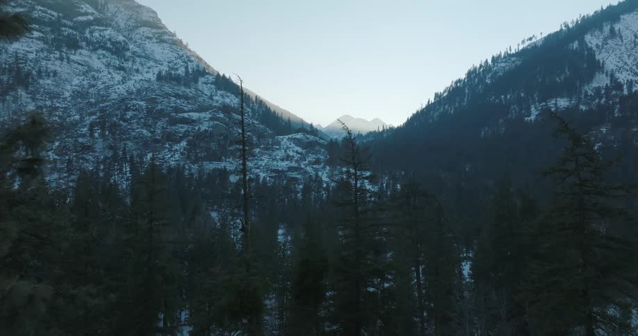 Reveal of a cold and rugged mountain valley past a rocky ridge covered with pine trees