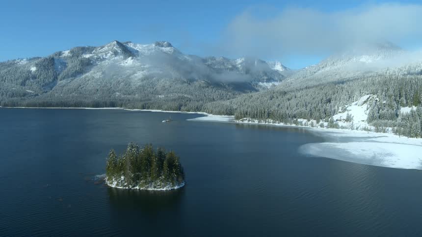 Subtle orbit around a tiny tree covered island in the middle of a cold and icy mountain lake