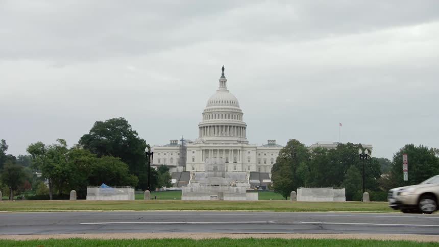 Automobiles travel on a road passing the capitol building under a cloudy sky