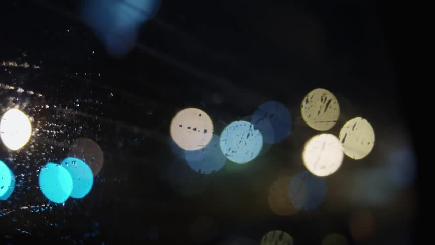 A city skyline is blurry through a rain covered vehicle window