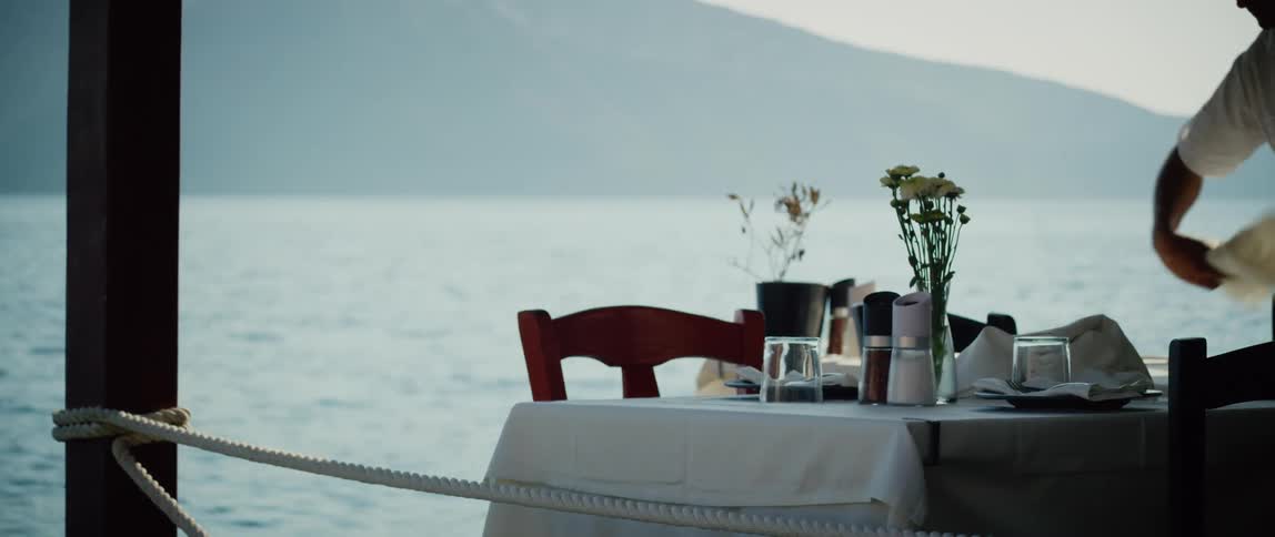 A waiter uses a napkin to dust off a dining table set overlooking the ocean