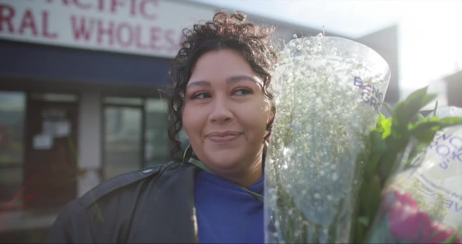 A woman stands outside a floral shop holding bouquets of flowers