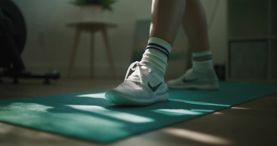 A person standing on a mat at home ties their shoe and gets ready to exercise