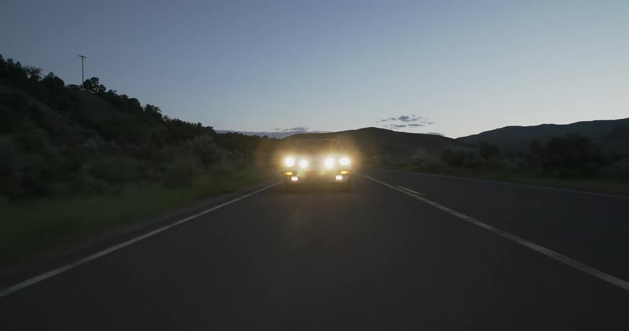 Car with headlights on drive on highway at dusk in the countryside