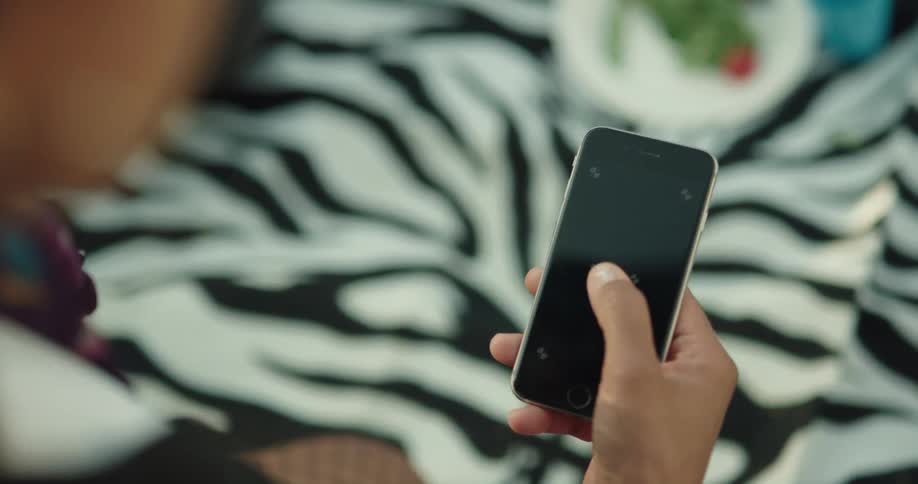 A teenager is holding a cell phone in their hand and moving their thumb across the screen