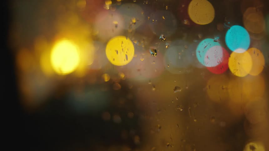 Vehicle headlights appear as a blur through rain covered windows