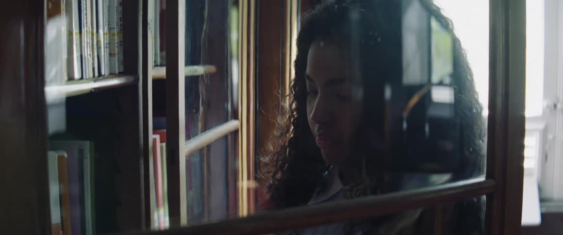A woman opens the glass door of a book cabinet and selects a book