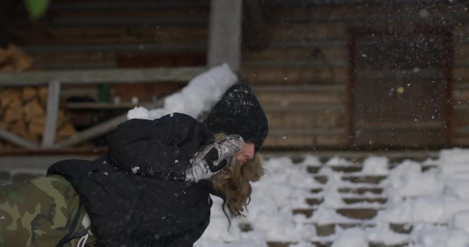 A woman jumps throwing a snowball and lands in the snow